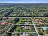 Aerial perspective of a multi-structure property featuring mature trees, expansive green space, and a paved driveway