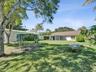 Expansive backyard featuring a sprawling lawn, mature trees, a detached storage structure, and a covered rear patio