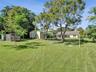 Expansive lawn featuring mature trees, a detached storage building, and a fenced enclosure
