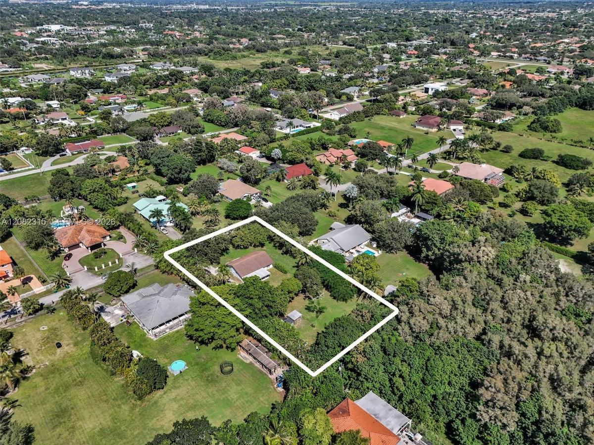 Aerial perspective of a property featuring a single-story residence, expansive lot, mature landscaping, and tree-lined perimeter