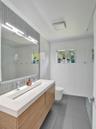 Floating vanity with a double-basin integrated countertop, vertical tile backsplash, full-width vanity mirror, and large-format floor tiling