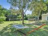 Expansive backyard featuring a large grass lawn, mature shade trees, and perimeter foliage