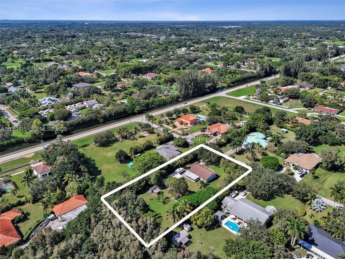 Aerial perspective of a property featuring expansive grounds, mature canopy trees, a sprawling lawn, and a multi-pitched roofline