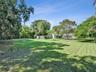 Expansive backyard featuring a manicured lawn, mature trees, and perimeter vegetation