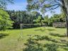 Expansive lawn area featuring mature trees and a detached wood-frame structure with wire mesh enclosure