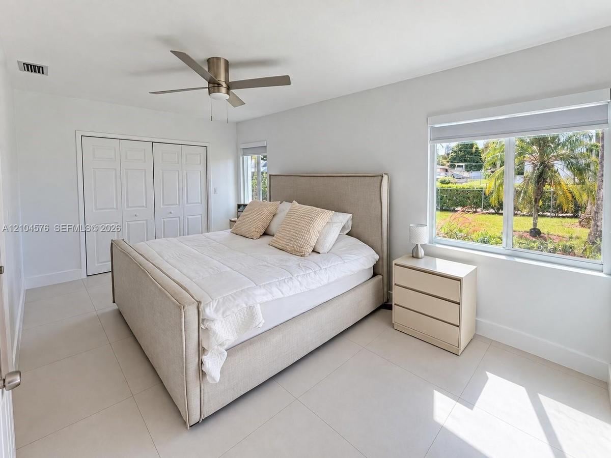 High-gloss white cabinetry, stainless steel French-door refrigerator, stone-surface countertop, recessed ceiling lighting, and large-format tile floor