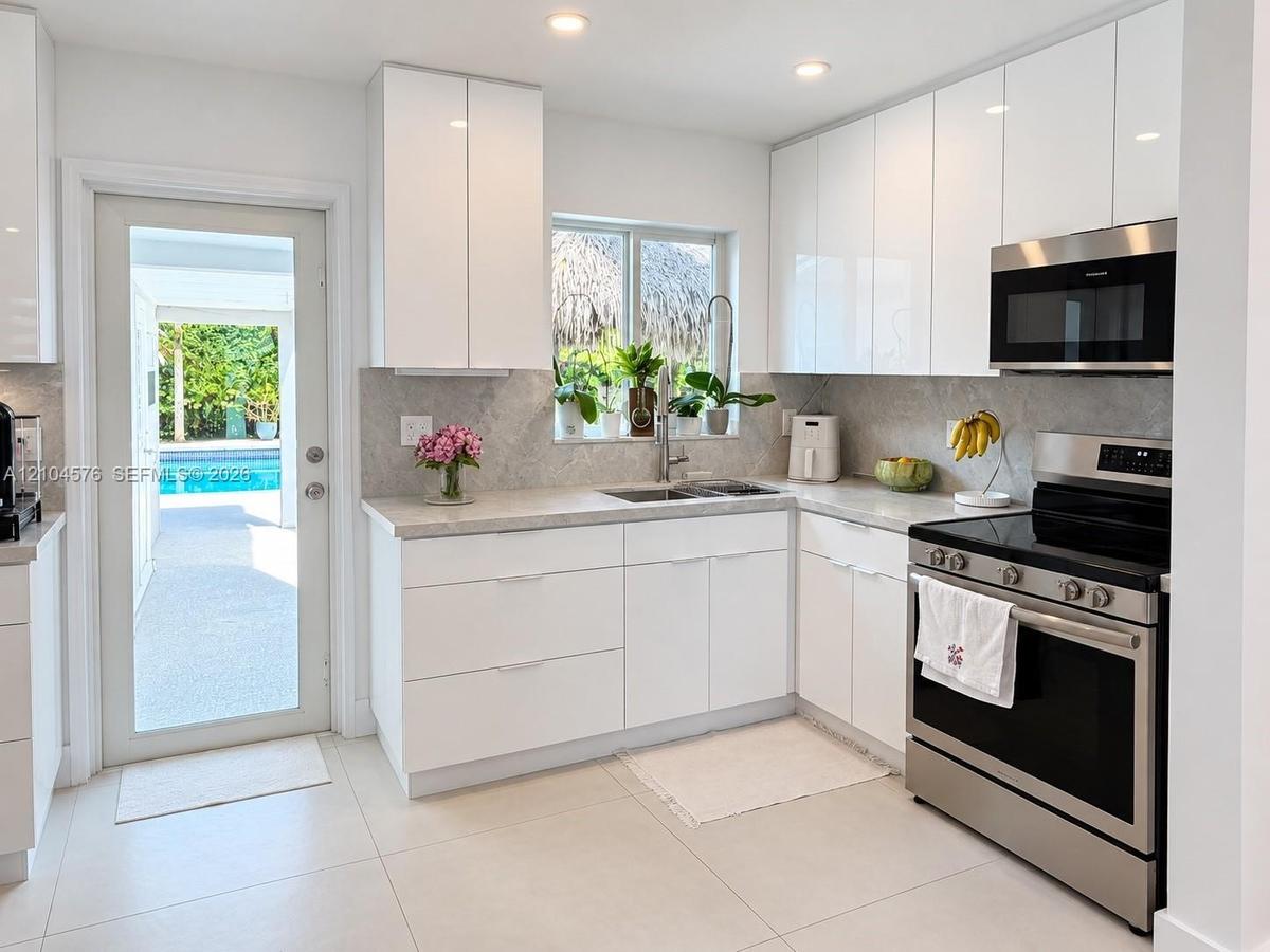 Contemporary interior featuring high-gloss white cabinetry, stainless steel refrigerator, large-format tile flooring, and recessed lighting