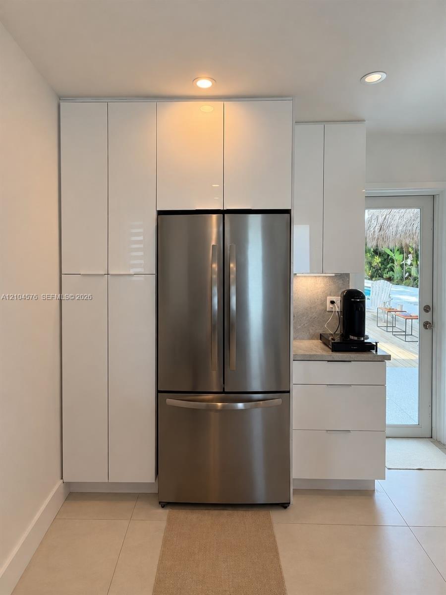 Large-format tile flooring, recessed lighting, and dual-shade window coverings featuring a glass-panel entry door
