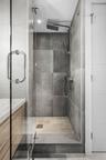 Walk-in shower featuring large-format gray tile walls, a dedicated rainfall showerhead, handheld sprayer, glass enclosure, and a stone-tiled floor