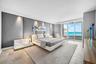 Full-height upholstered wall paneling with integrated accent lighting, tile flooring, and floor-to-ceiling glass sliding doors opening to an ocean bac