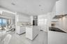 Modern kitchen featuring high-gloss cabinetry, stone countertops, integrated appliances, a central island, and large-format tile flooring