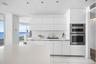 Contemporary kitchen featuring high-gloss white cabinetry, integrated stainless steel double wall ovens, solid-surface countertops, recessed ceiling l