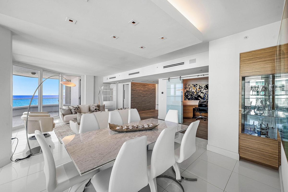 Open-concept living space featuring high-gloss tile flooring, recessed tray ceiling lighting, built-in wooden cabinetry with glass-front shelving, sli