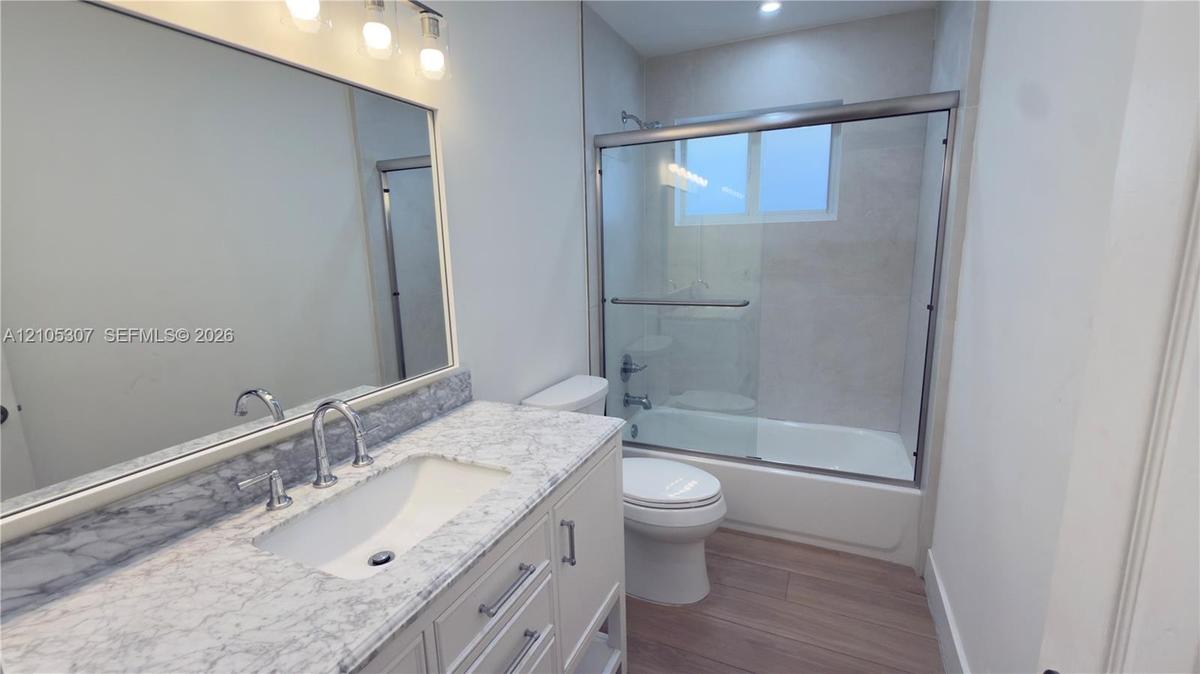 Bathroom with tub, eaturing a vanity with a stone-finish countertop, undermount sink, chrome faucet, large wall-mounted mirror with integrated lightin