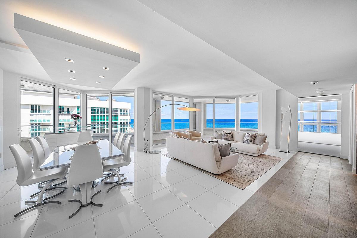 Open-concept interior featuring floor-to-ceiling glass windows, ocean scenery, white tile flooring, and a recessed ceiling architectural detail with i