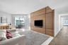 Custom floor-to-ceiling wood-panel accent wall with integrated television mount, expansive floor-to-ceiling glass doors, and polished stone flooring
