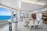 Expansive floor-to-ceiling windows, polished tile flooring, tiered tray ceiling with recessed lighting, integrated glass and stone-finish bar, and sli