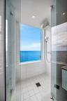 Walk-in shower featuring white tiled walls, a floor-to-ceiling window with water frontage, a rain-style shower head, and a handheld fixture