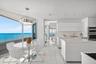Floor-to-ceiling glass paneling, high-gloss white cabinetry, center island with stone countertop, large-format tile flooring, and integrated stainless