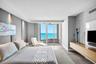 Floor-to-ceiling glass sliding doors opening to a balcony, wall-to-wall upholstered headboard paneling, wall-mounted wood-finish media console, and la