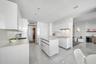 Minimalist kitchen featuring high-gloss white cabinetry, quartz countertops, a central island, recessed ceiling lighting, and polished tile flooring