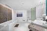 Bathroom featuring a freestanding white soaking tub, textured stone accent wall, dual-sink vanity with stone countertop, frameless glass-enclosed show