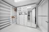 Custom storage closet featuring floor-to-ceiling white shelving, integrated multi-drawer cabinetry, full-length mirror panels, and metallic hardware