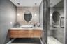 Floating wood-finish vanity with a vessel sink and stone countertop, pebble-texture accent wall, dual pendant lighting, and a glass-enclosed shower wi
