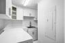 Laundry area featuring white cabinetry, integrated open shelving, a stainless steel sink with a high-arc faucet, and solid-surface countertops