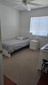 Neutral-toned carpeting, ceiling-mounted paddle fan, and large window with horizontal blinds