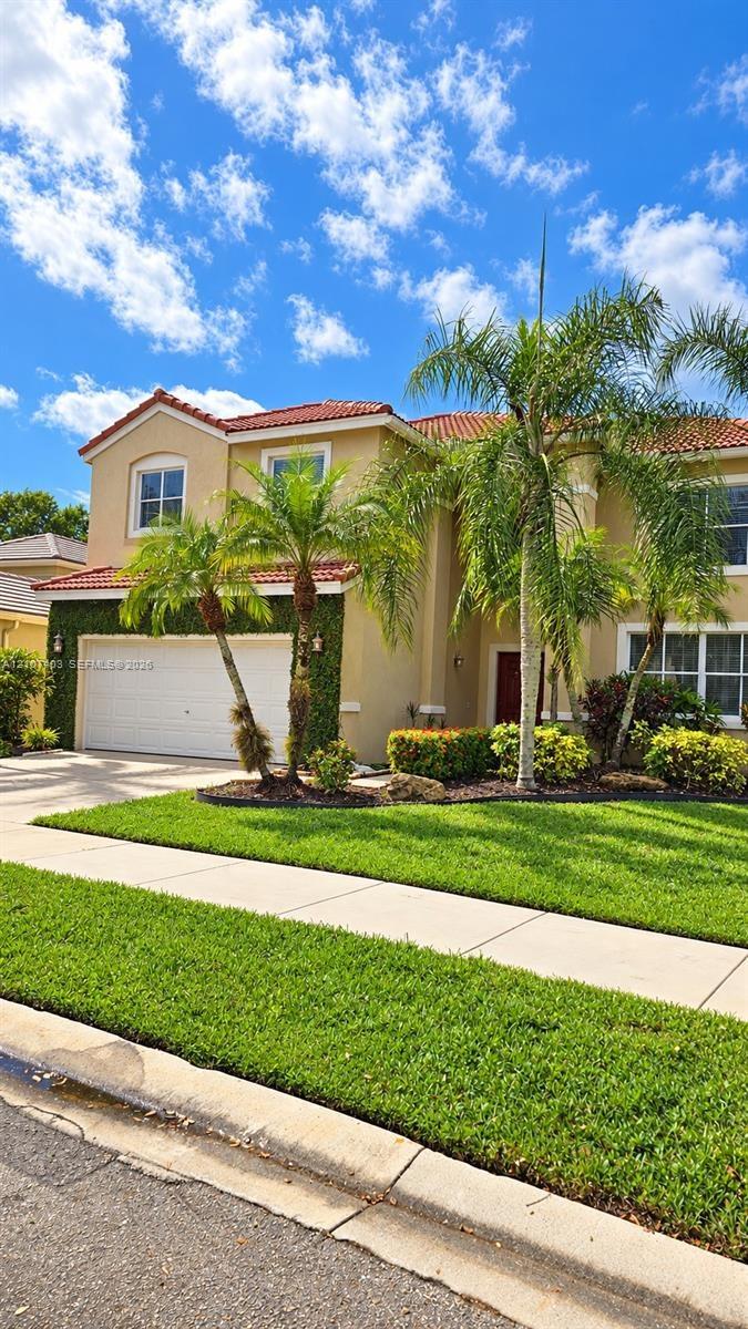 Two-story residence featuring a terracotta-tiled roof, stucco exterior, multi-pane windows, and a paved driveway leading to an attached two-car garage