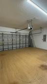 Enclosed garage featuring wood-finish flooring, metal sectional overhead door, ceiling-mounted automatic door opener, and integrated electrical servic