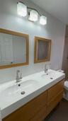 Double vanity with a white integrated sink countertop, wood-finish cabinetry, two square framed mirrors, and a brushed nickel three-light fixture