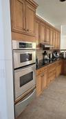 Kitchen featuring natural-finish wood cabinetry, dark stone countertops, tile backsplash, and built-in stainless steel double wall ovens