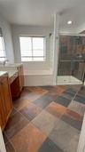 Bathroom featuring wood-finish cabinetry, a white countertop with an integrated sink, a deep soaking tub, a multi-tone tile floor, and a walk-in showe