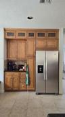 Custom built-in cabinetry featuring glass-panel upper doors, integrated stainless steel side-by-side refrigerator, stone-surfaced countertop, and tile
