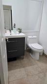 Dark gray dual-drawer vanity with a white countertop, rectangular integrated basin, one-piece toilet, large wall-mounted mirror, and tile flooring