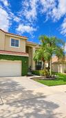 Stucco exterior with a tiled roof, integrated garage, concrete driveway, and manicured landscaping featuring mature palm trees