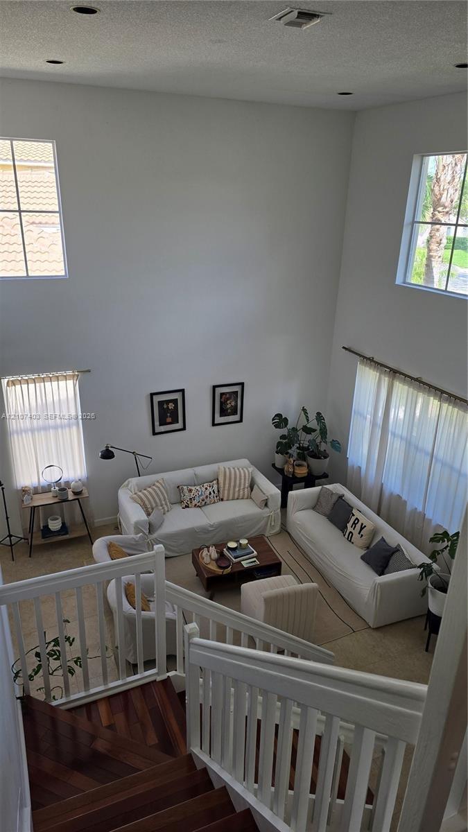 High-ceiling living area featuring multi-level windows, wood-finish staircase treads, and white vertical baluster railing