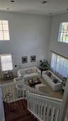 High-ceiling living area featuring multi-level windows, wood-finish staircase treads, and white vertical baluster railing
