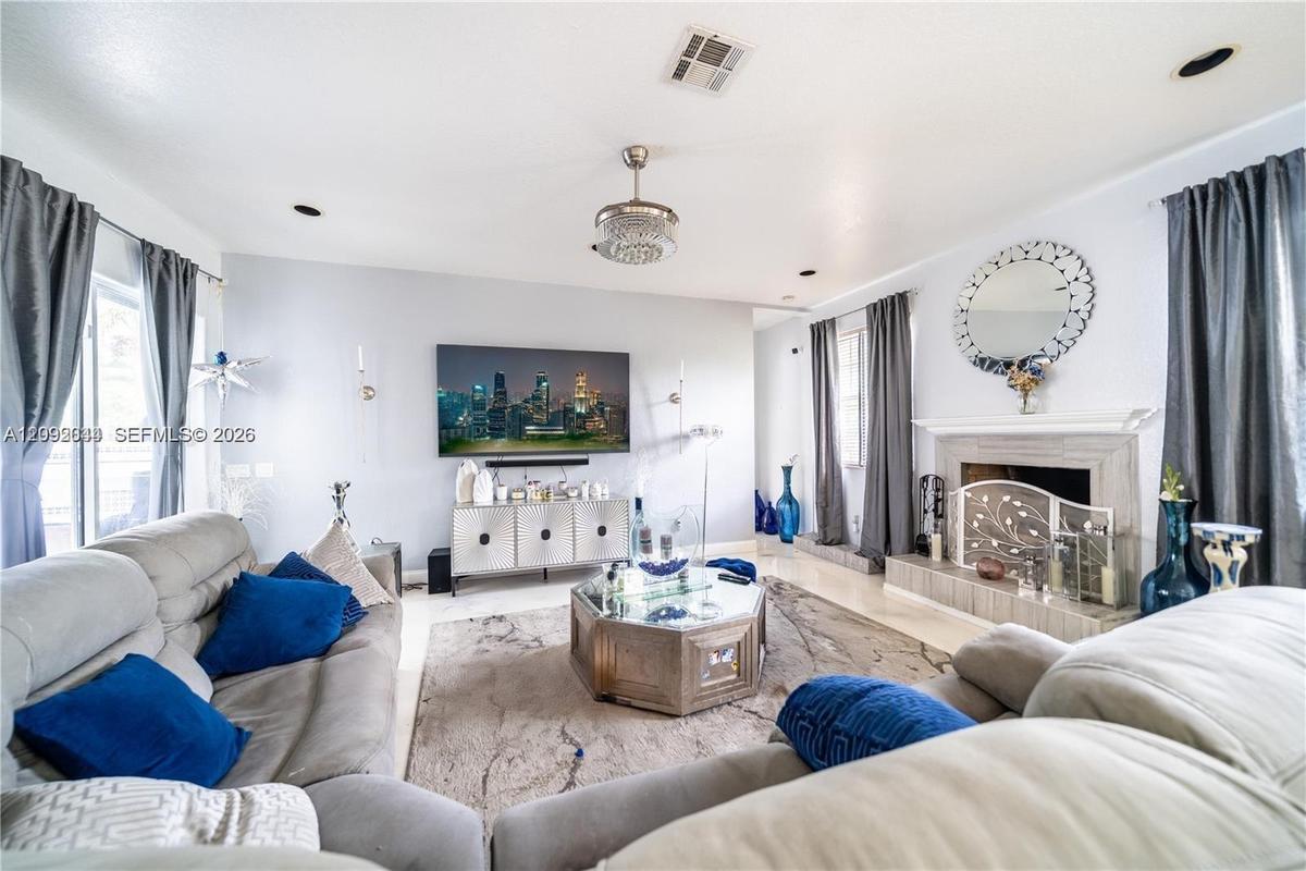 Living area featuring a fireplace with a stone-finish surround, recessed lighting, a decorative ceiling fan, and large windows with integrated drapery