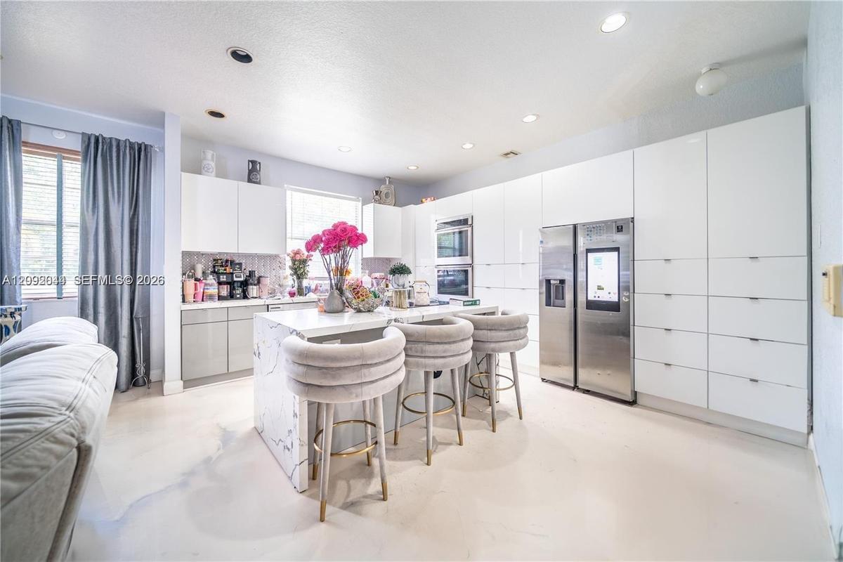 Kitchen featuring high-gloss white flat-panel cabinetry, a central island with a stone-finish waterfall edge, integrated stainless steel appliances, a