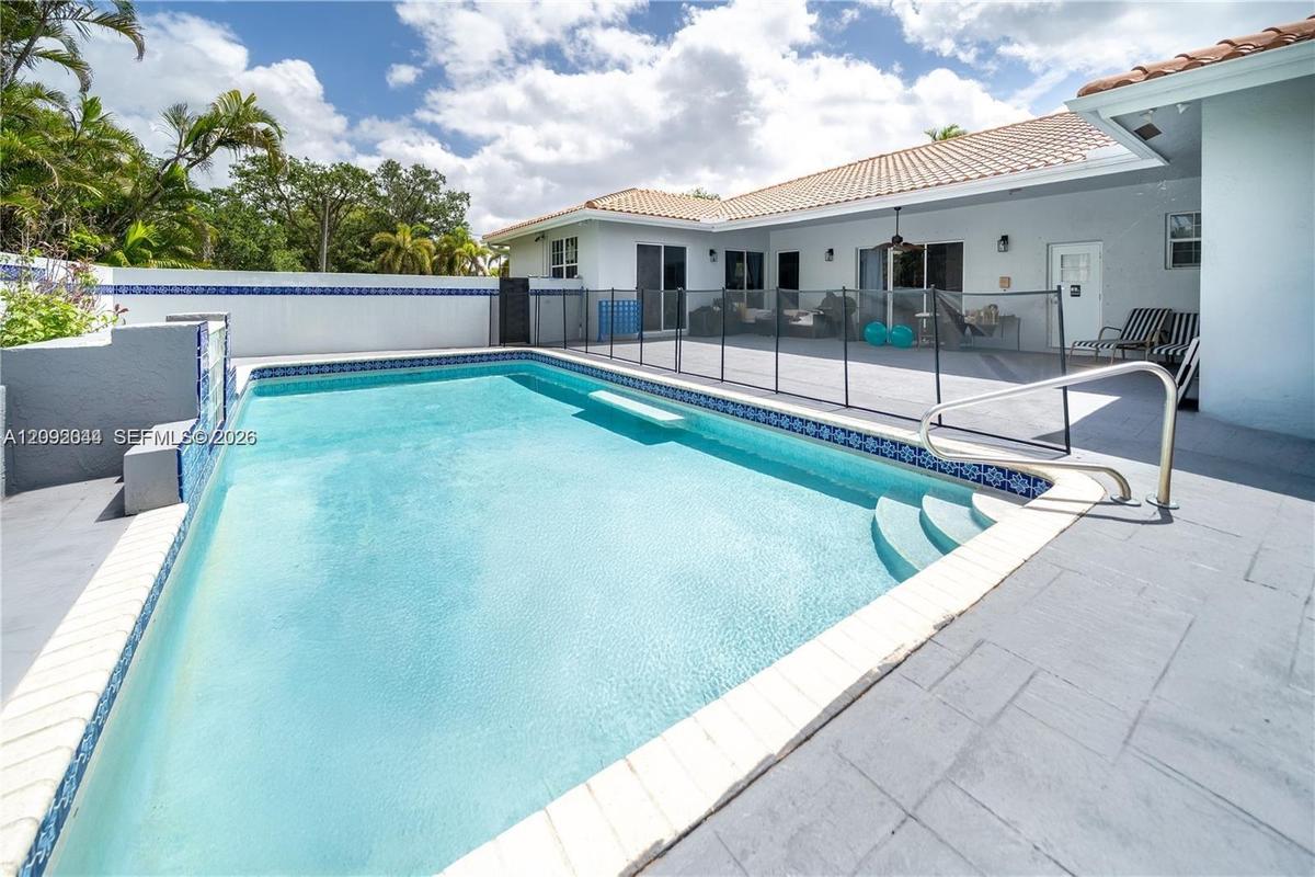 In-ground swimming pool featuring a tiled waterline, integrated steps, and a concrete paver deck enclosed by a perimeter wall