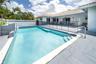 In-ground swimming pool featuring a tiled waterline, integrated steps, and a concrete paver deck enclosed by a perimeter wall
