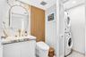 Stone-surround vanity with a circular mirror and gold-tone faucet, complemented by vertical slat wood-finish wall paneling, a low-profile toilet, and 