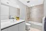 Bathroom featuring a floating vanity with a stone countertop, an integrated rectangular sink, a frameless glass shower panel, and stone-tile tub surro