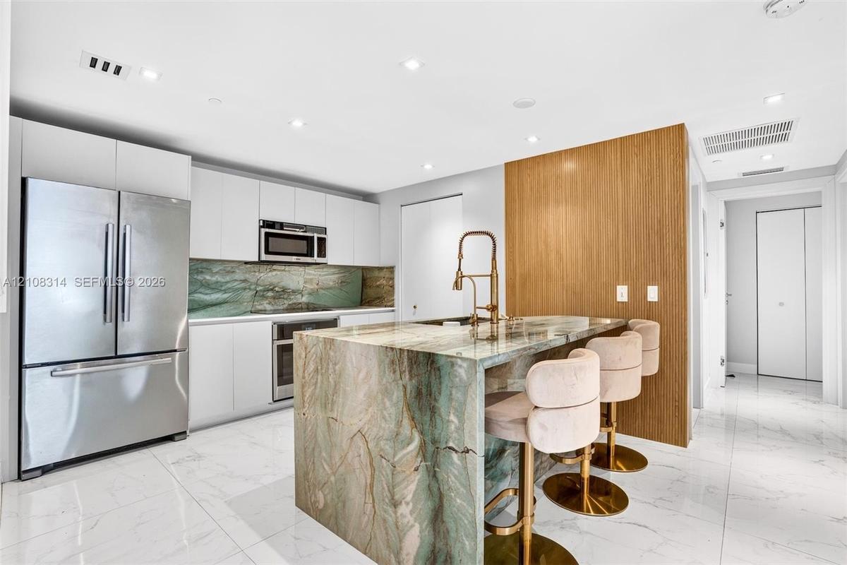 Kitchen featuring flat-panel white cabinetry, stone-clad waterfall island, matching stone backsplash, wood-finish accent wall, and stainless steel app
