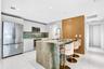 Kitchen featuring flat-panel white cabinetry, stone-clad waterfall island, matching stone backsplash, wood-finish accent wall, and stainless steel app