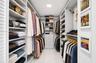 Custom walk-in closet featuring extensive built-in white shelving, integrated clothing rods, a central storage tower with four pull-out drawers, and p