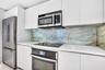 Kitchen featuring flat-panel white cabinetry, stone-patterned slab backsplash, quartz countertops, and stainless steel appliances including a built-in